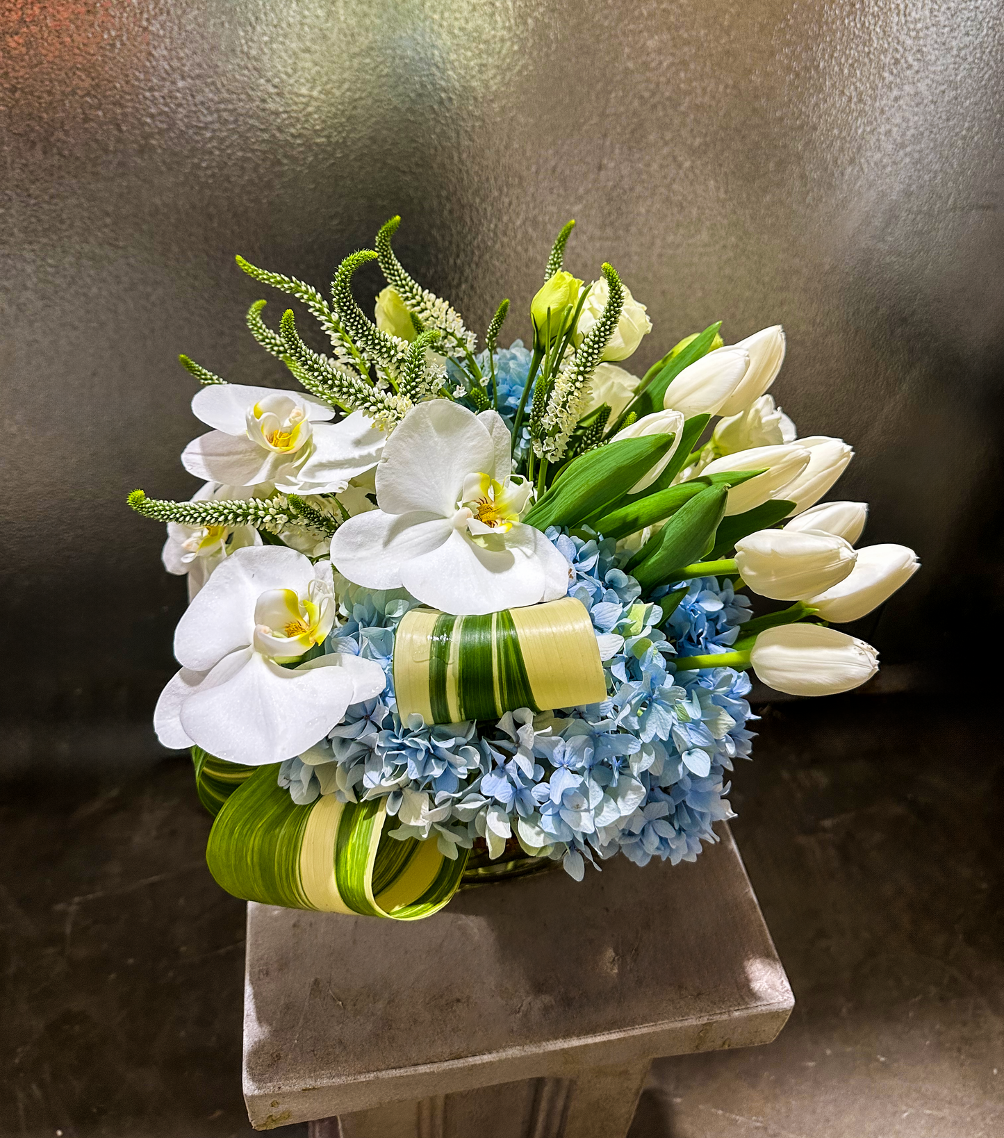 A luxurious floral arrangement featuring pristine white orchids, delicate tulips, and soft hydrangeas with green accents. The white and green tones give a fresh, elegant look perfect for sophisticated events in Houston. Ideal for VIP floral services or high-end gatherings.