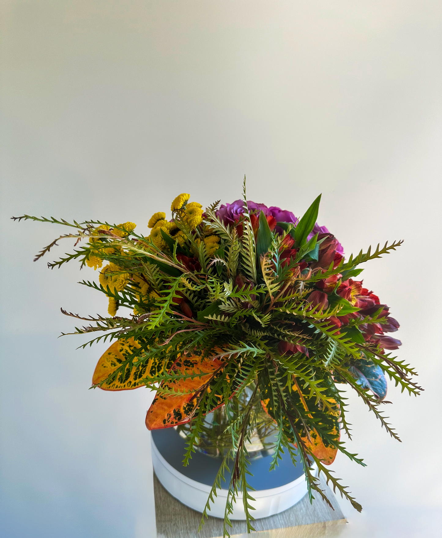 A lush, foliage-heavy arrangement showcasing a variety of greens with hints of lavender roses and chrysanthemums peeking through. This unique design makes a bold statement, ideal for Houston-based gatherings that seek elegance with a natural twist.