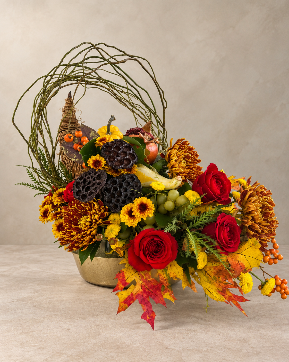 Wide side view of the woven cornucopia horn surrounded by red roses, chrysanthemums, fruit, lotus pods, looping branches and autumn foliage.