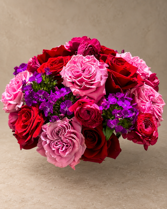 Passion bouquet with red, hot-pink, blush and lavender roses accented by clusters of vivid purple dianthus.