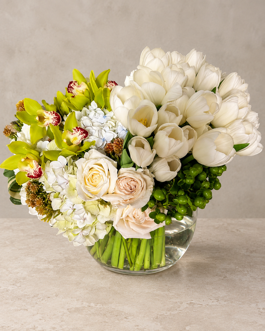 Tulip Clusters arrangement with white tulips, green cymbidium orchids, white hydrangea, cream roses and hypericum berries in a clear glass vase.