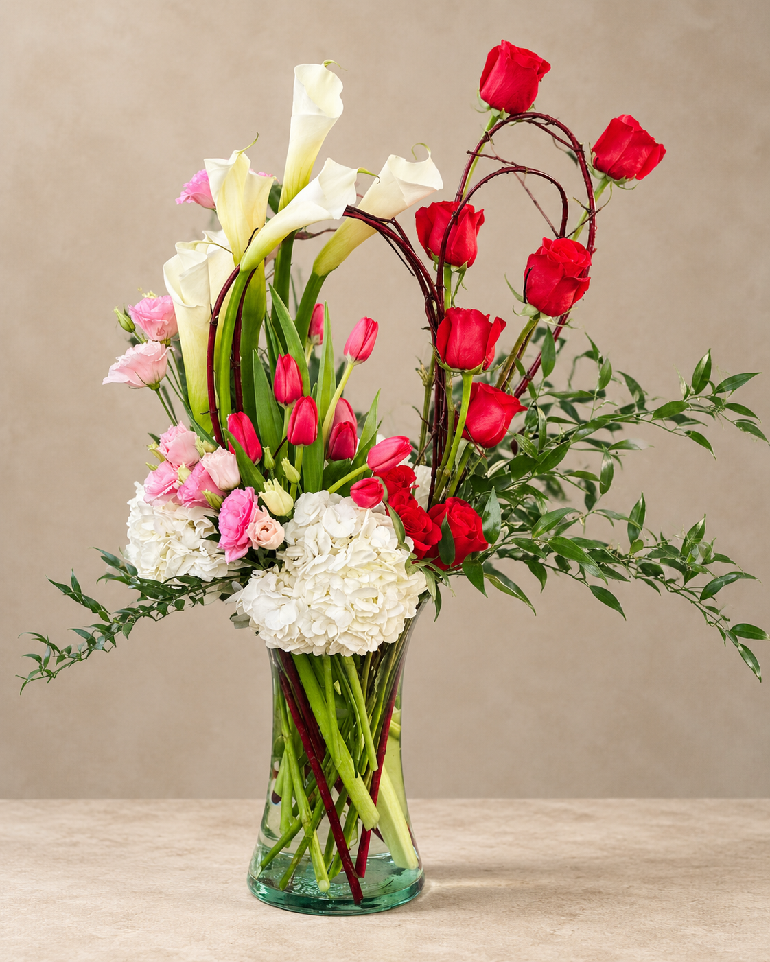 Souls in Love arrangement with red roses, white calla lilies, red tulips, pink lisianthus and white hydrangea in a clear glass vase.