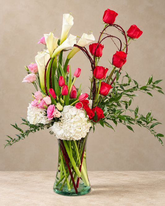 Souls in Love arrangement with red roses, white calla lilies, red tulips, pink lisianthus and white hydrangea in a clear glass vase.