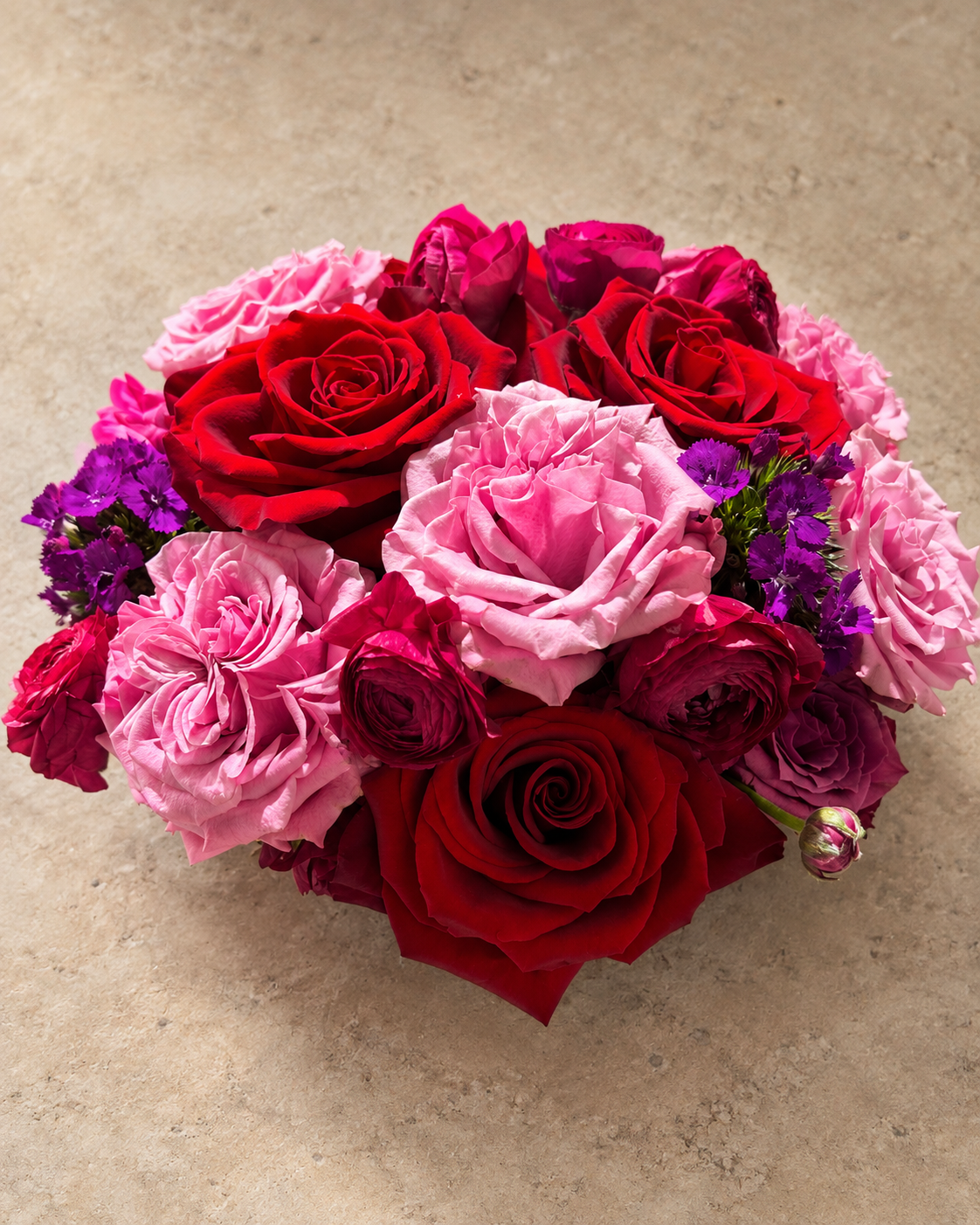 Overhead view of the Passion bouquet with red and pink roses, ruffled magenta blooms and purple dianthus accents.