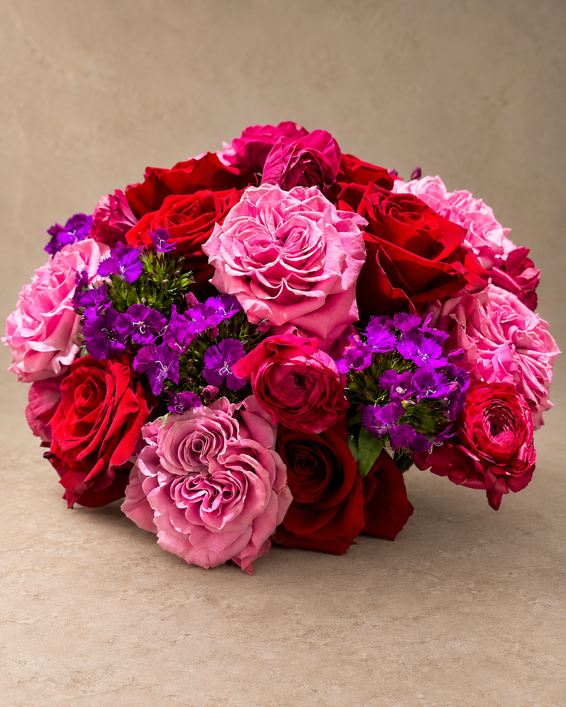 Passion bouquet with red, hot-pink, blush and lavender roses accented by clusters of vivid purple dianthus.