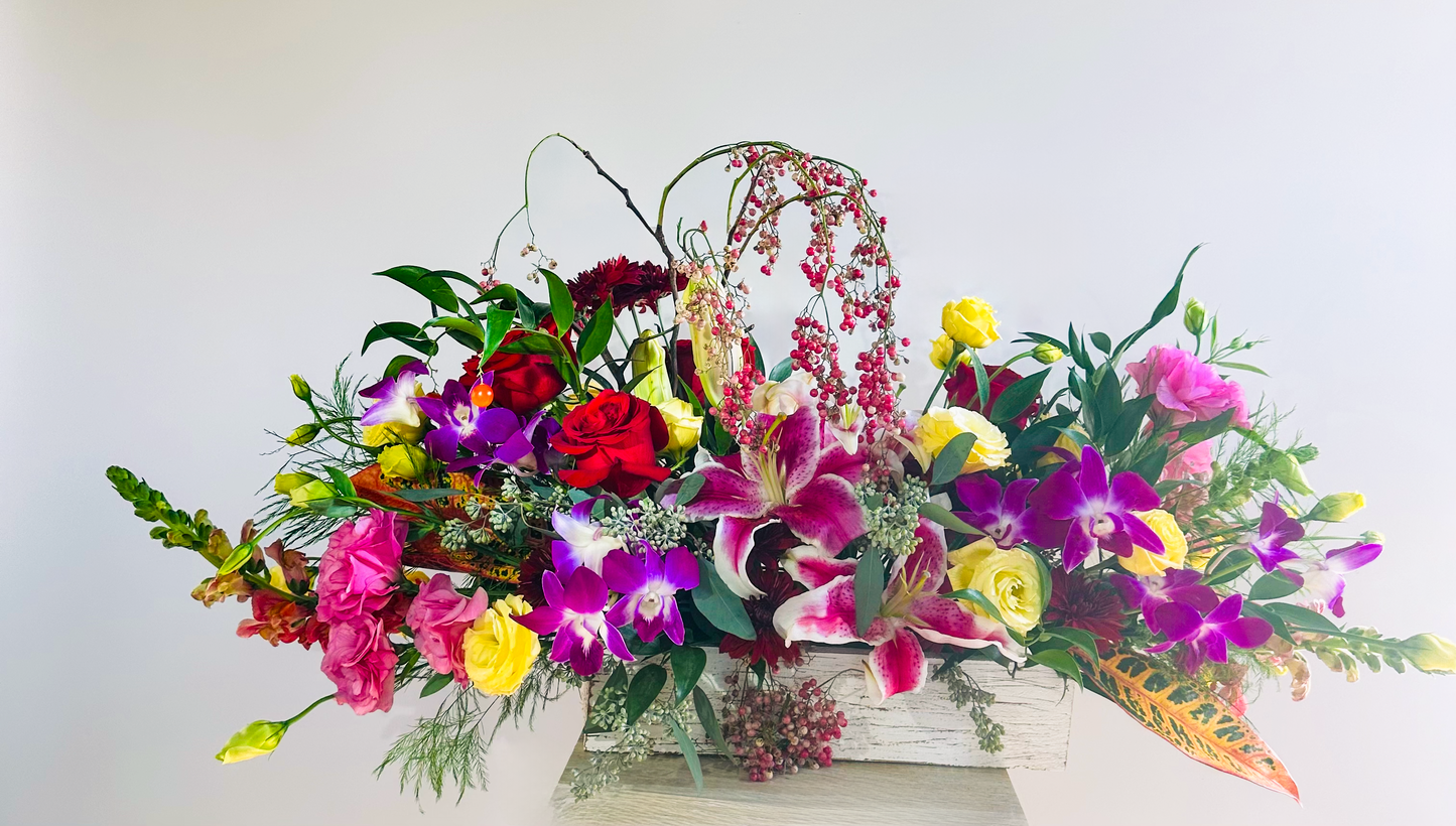 Colorful floral display featuring red roses, purple orchids, yellow spray roses, pink lisianthus, and lilies in a rustic container, ideal for Houston events and celebrations.