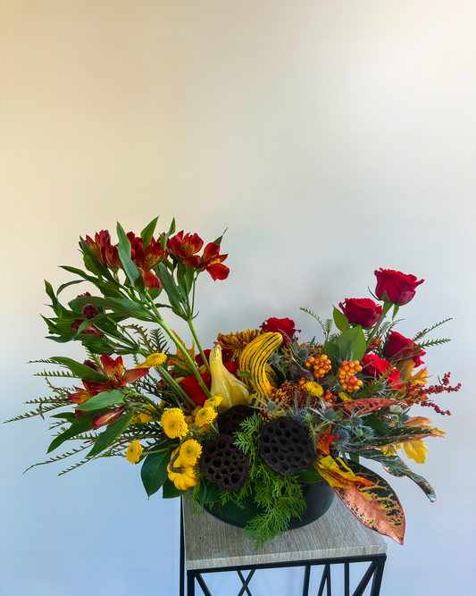 Festive fall floral arrangement with red roses, yellow chrysanthemums, croton leaves, gourds, and lotus pods - VIP Floristry, Houston.