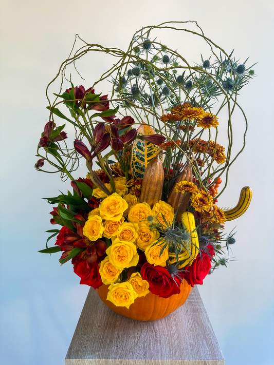 Unique autumn arrangement in a pumpkin vase, featuring yellow and red roses, chrysanthemums, and dried thistle branches. Perfect for adding a touch of seasonal beauty, crafted by VIP Floristry in Houston.