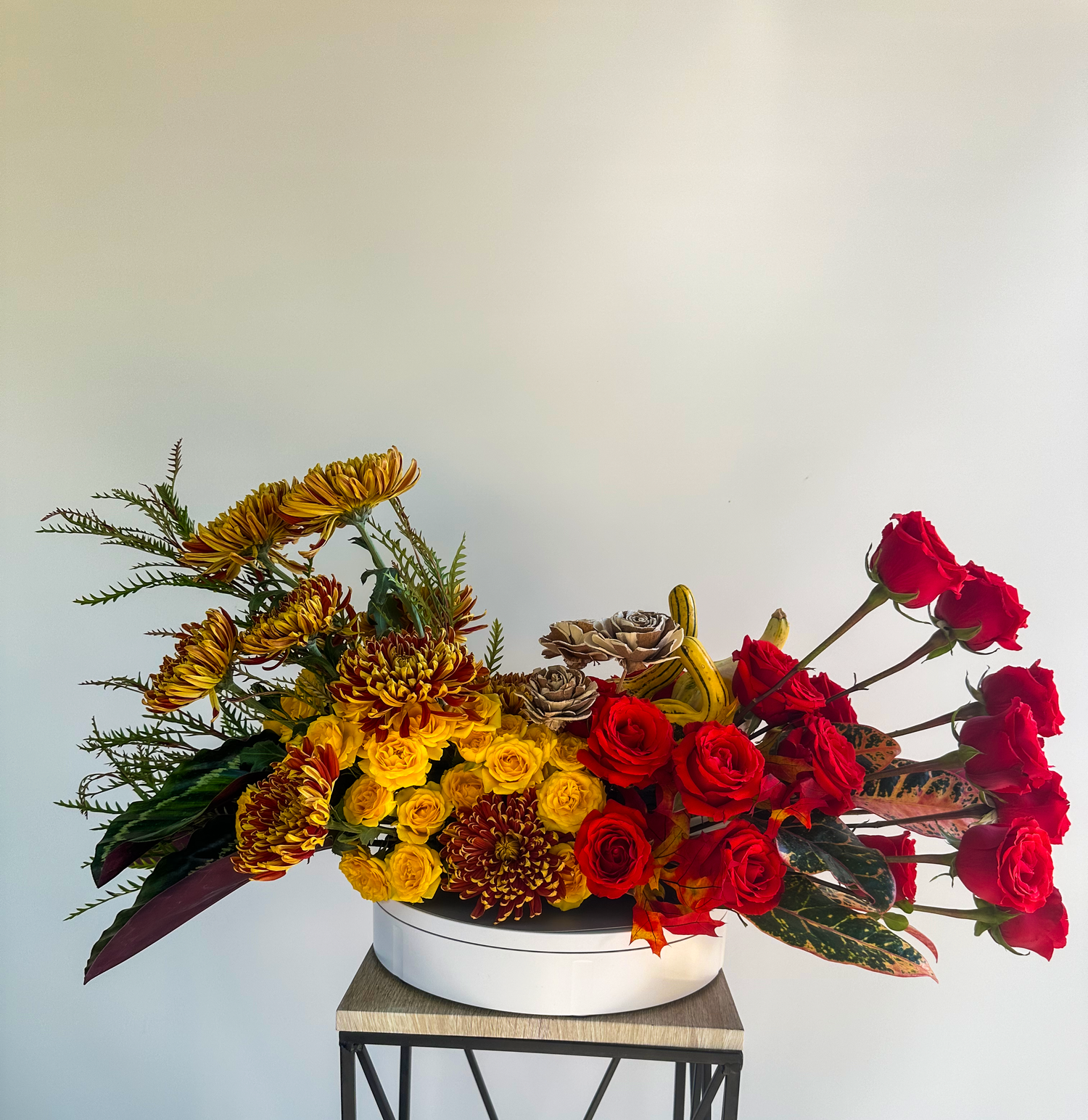 Unique floral arrangement featuring vibrant red roses, yellow chrysanthemums, and greenery in a modern white container, showcasing VIP Floristry's custom luxury floral designs in Houston.