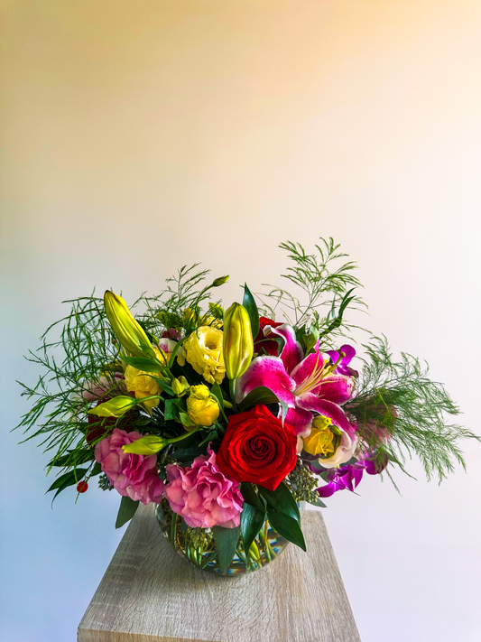 Elegant floral arrangement with vibrant red, pink, and yellow blooms, featuring lilies, roses, and hydrangeas in a clear vase, designed by Houston’s luxury florist, VIP Floristry.