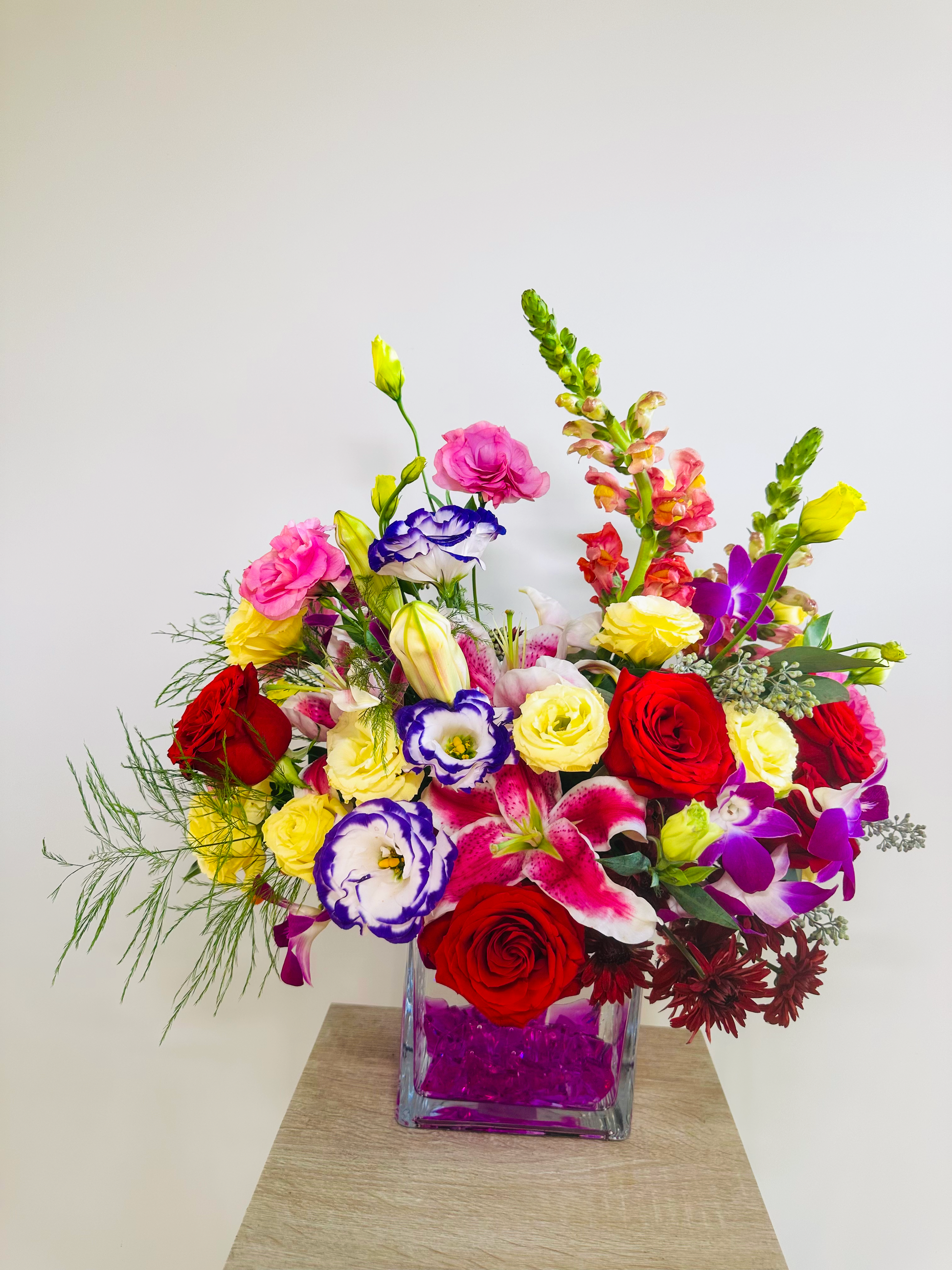 Luxurious flower arrangement with red roses, pink stargazer lilies, yellow snapdragons, and purple lisianthus in a glass vase, capturing vibrant colors for Houston floral decor.