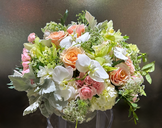 A beautifully arranged floral bouquet featuring soft peach roses, white orchids, delicate pink roses, and lush greenery. This elegant blend of colors and textures creates a soothing and luxurious ambiance, perfect for special occasions in Houston.