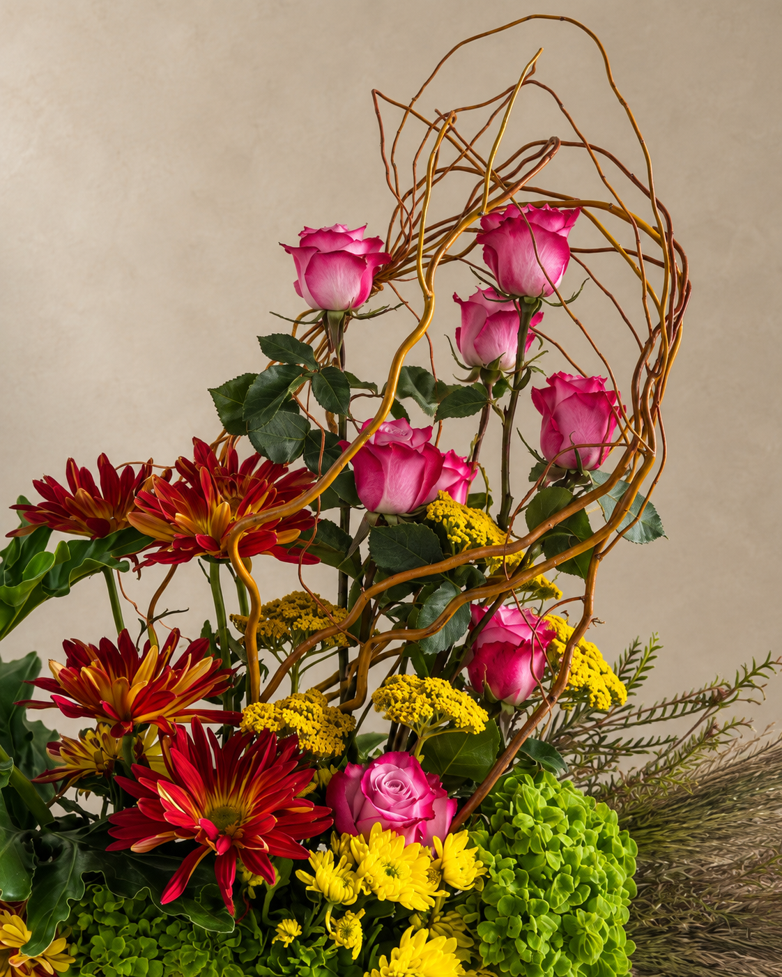 Close detail of pink roses framed by sculptural curly willow, red-bronze chrysanthemums, yellow yarrow and green hydrangea.