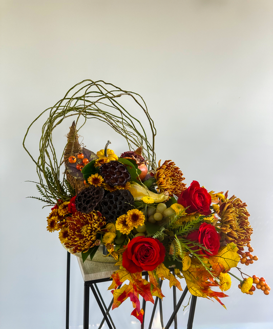 Elegant cornucopia floral design with twisted willow accents, showcasing red roses, yellow chrysanthemums, and seasonal foliage, ideal for autumnal celebrations.