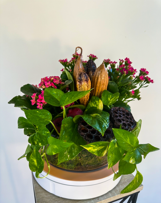 arden-inspired arrangement in a glass vase featuring lush pothos leaves, pink kalanchoe blossoms, and rustic dried pods, creating a natural look for elegant interiors in Houston.