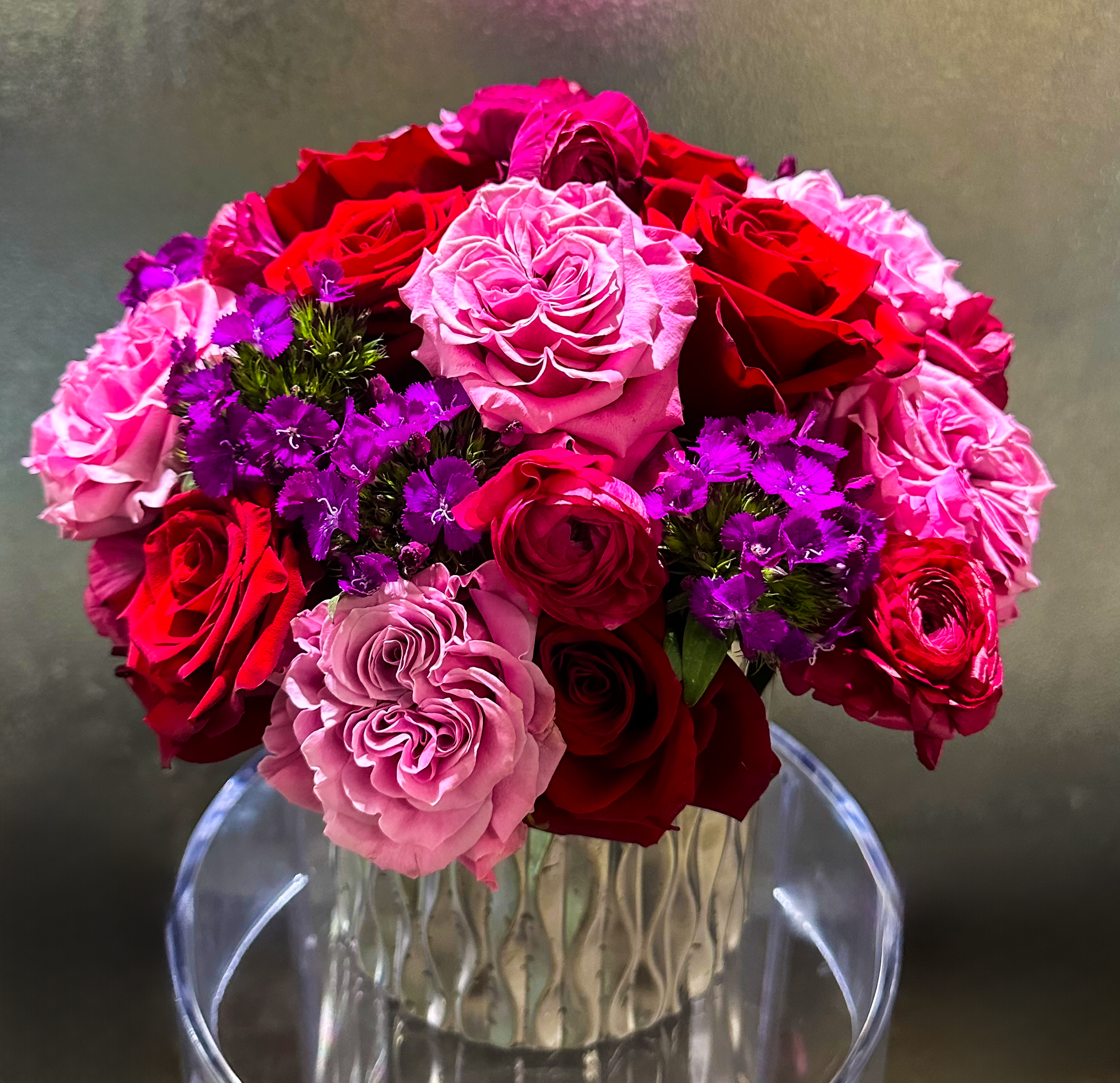 Luxurious floral arrangement in vibrant shades of red, pink, and purple roses with dianthus, displayed in an elegant textured vase by VIP Floristry, Houston.