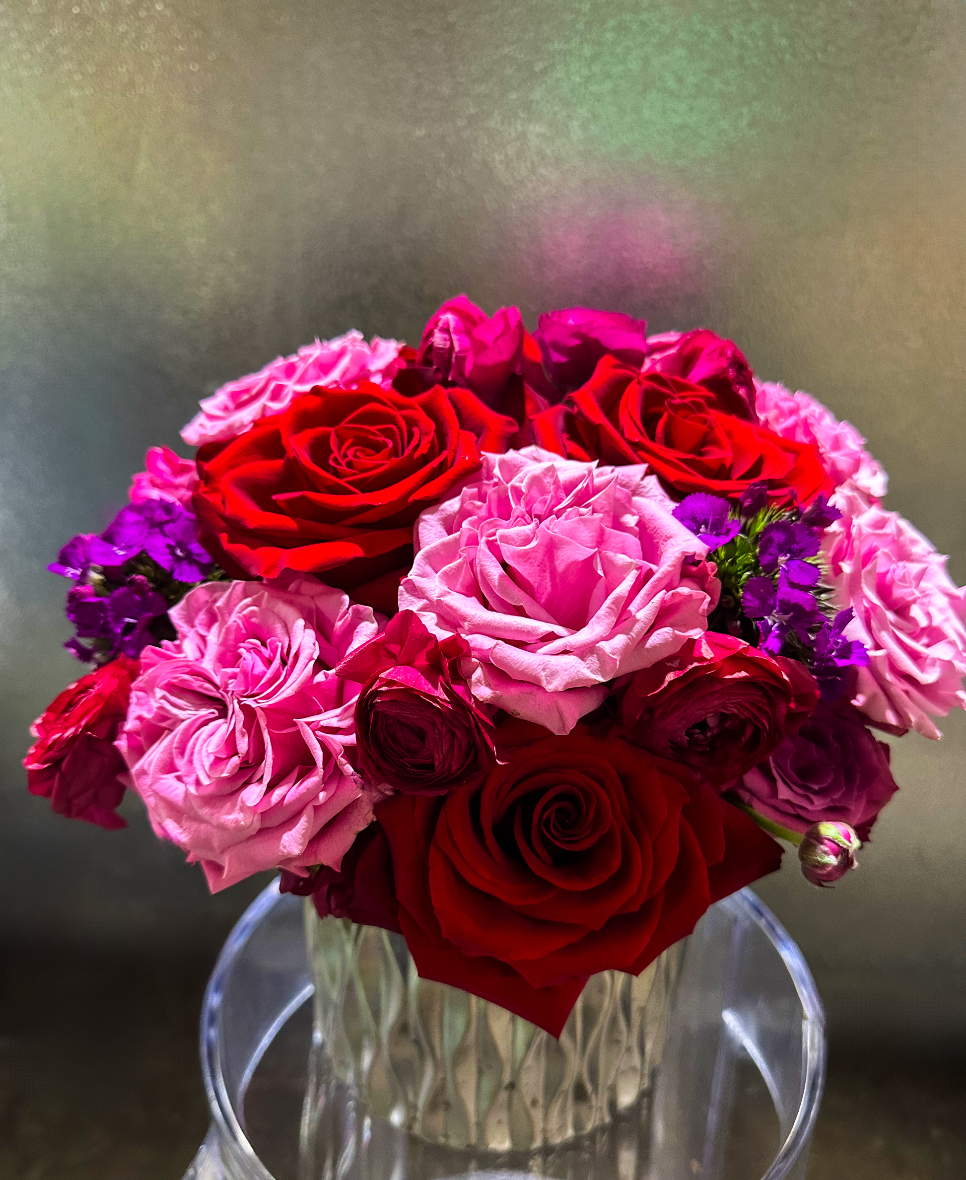 Close-up of an opulent red, pink, and purple rose arrangement, featuring dianthus accents, in a decorative vase by VIP Floristry, Houston.