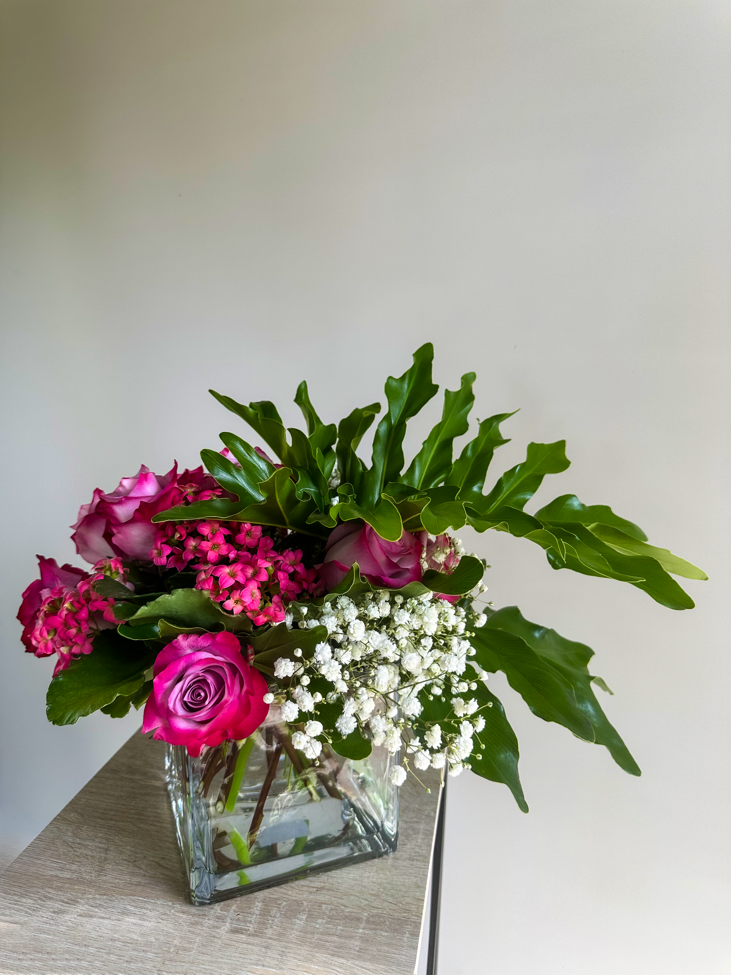 Elegant floral arrangement with vibrant pink roses, white baby's breath, and lush green leaves in a glass cube vase - VIP Floristry, Houston