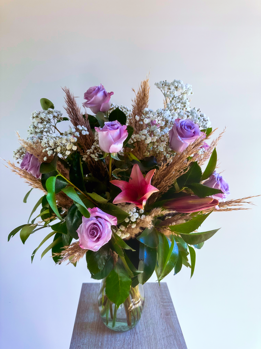 Elegant floral arrangement with lavender roses, pink lilies, baby's breath, and pampas grass in a clear glass vase. Perfect for adding a touch of luxury to Houston events and interiors.