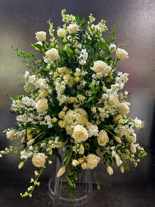 An elegant and grand floral arrangement composed of white roses, tulips, hydrangeas, and delicate lisianthus, paired with lush greenery. This luxurious arrangement features a mix of soft white blooms cascading gracefully, creating a serene and sophisticated display.