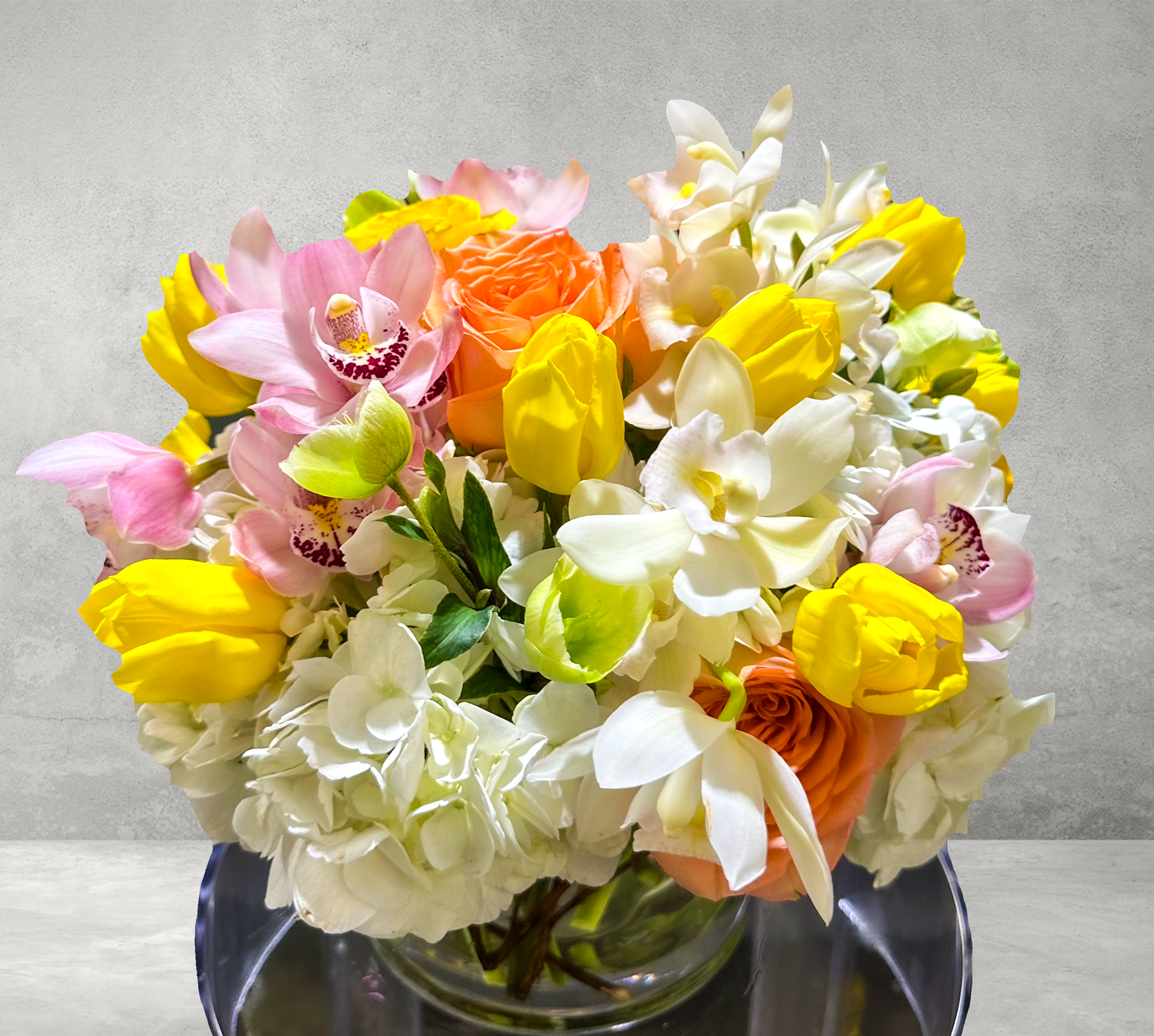 Close-up of a sunny arrangement with yellow tulips, white orchids, peach roses, and hints of pink, artfully arranged to convey a joyful and luxurious vibe. Ideal for events or gifts in the Houston area, capturing the essence of springtime elegance.